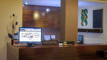 Una recepción con un monitor de computadora mostrando un anuncio de propiedad, un letrero que dice "RECEPTION" y una planta decorativa.