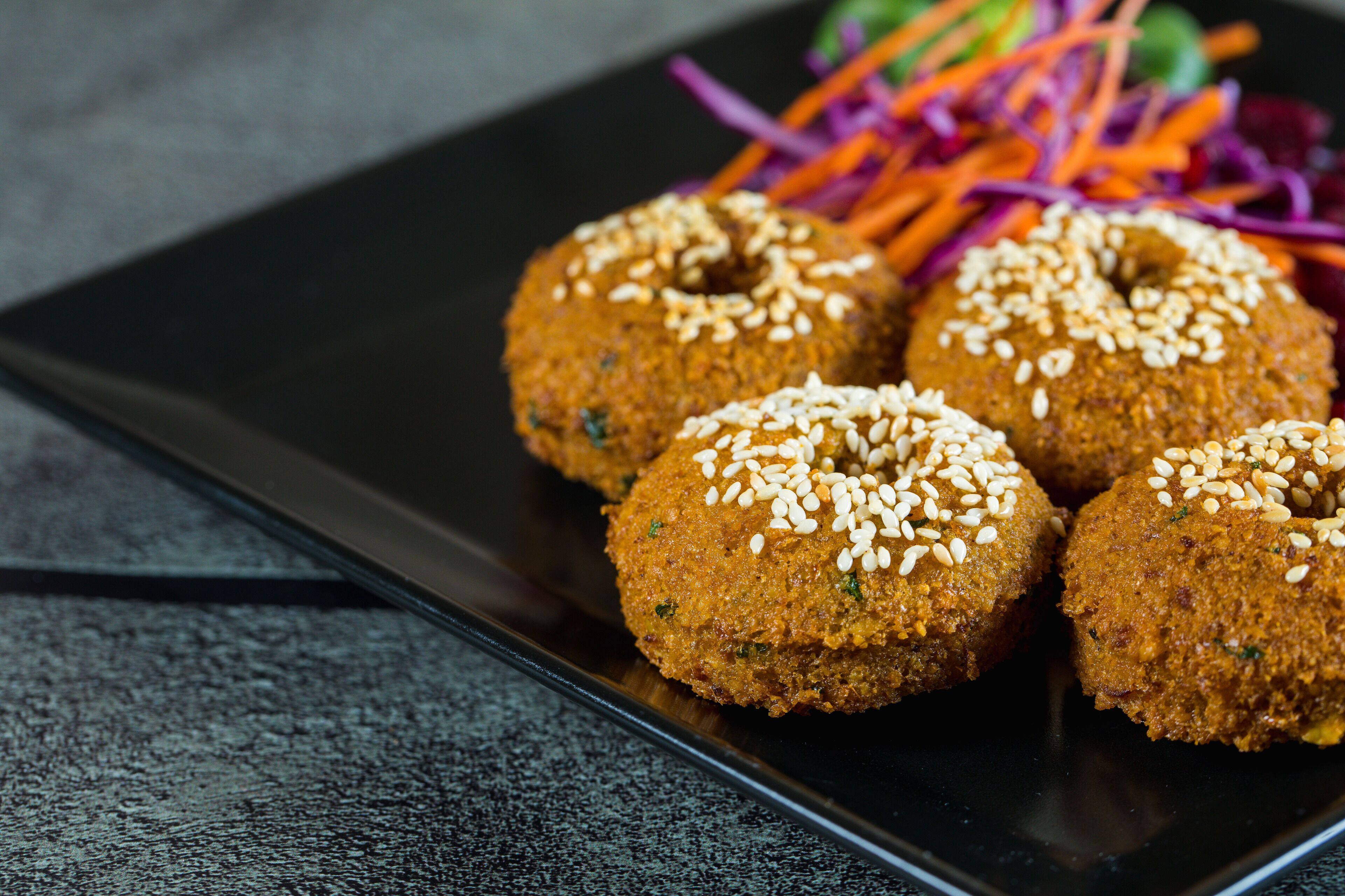 A plate of falafel balls garnished with sesame seeds and served with a side of mixed vegetables.