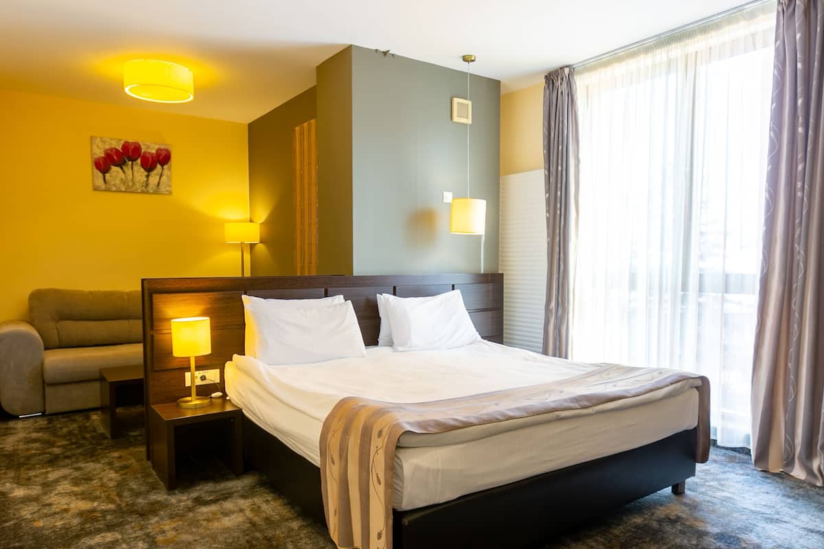 A hotel room with a large bed, bedside tables, a sofa, and a window with curtains.