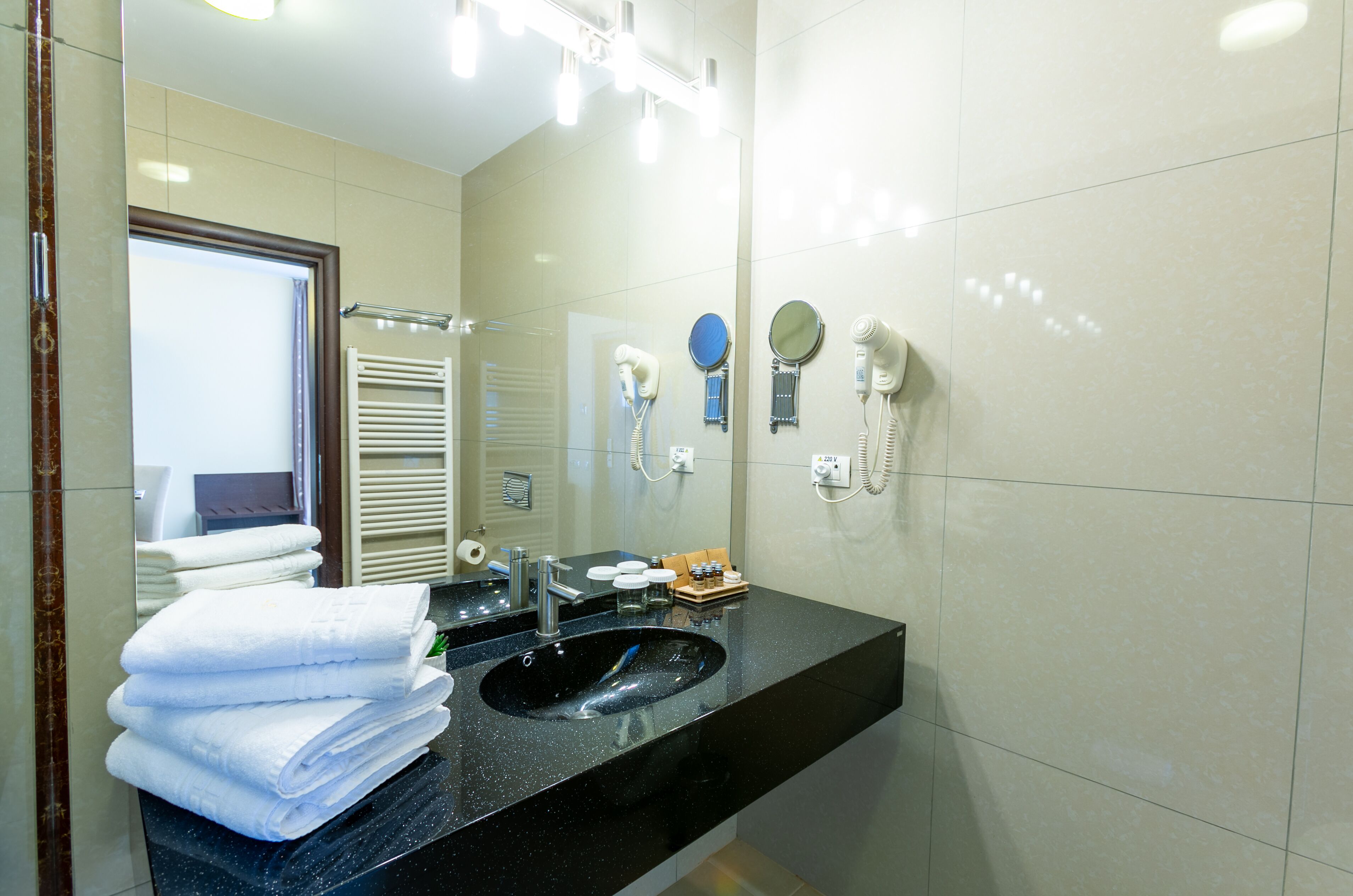 A modern bathroom with a black sink, white towels, a mirror, and a hairdryer.