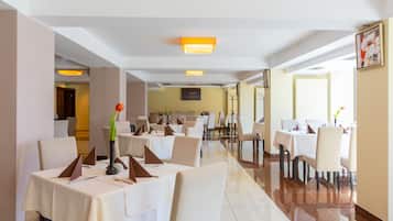 A hotel dining area with multiple tables, chairs, and a vase with flowers.