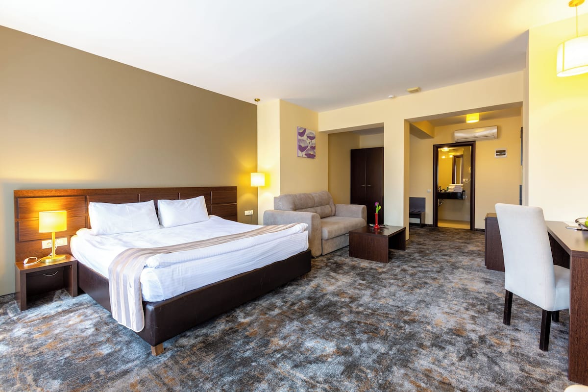 A hotel room with a large bed, a desk, a chair, a sofa, and a small table.