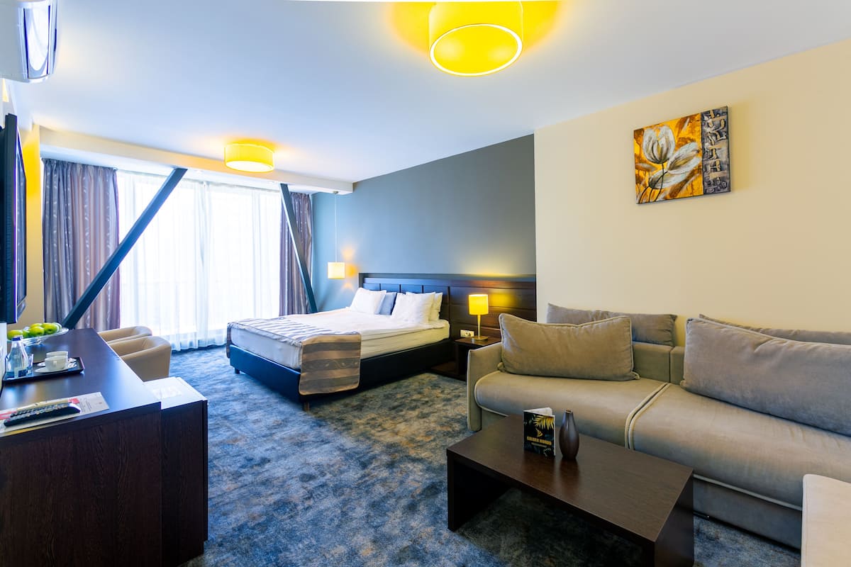 A hotel room with a bed, a sofa, a desk, and a painting on the wall.