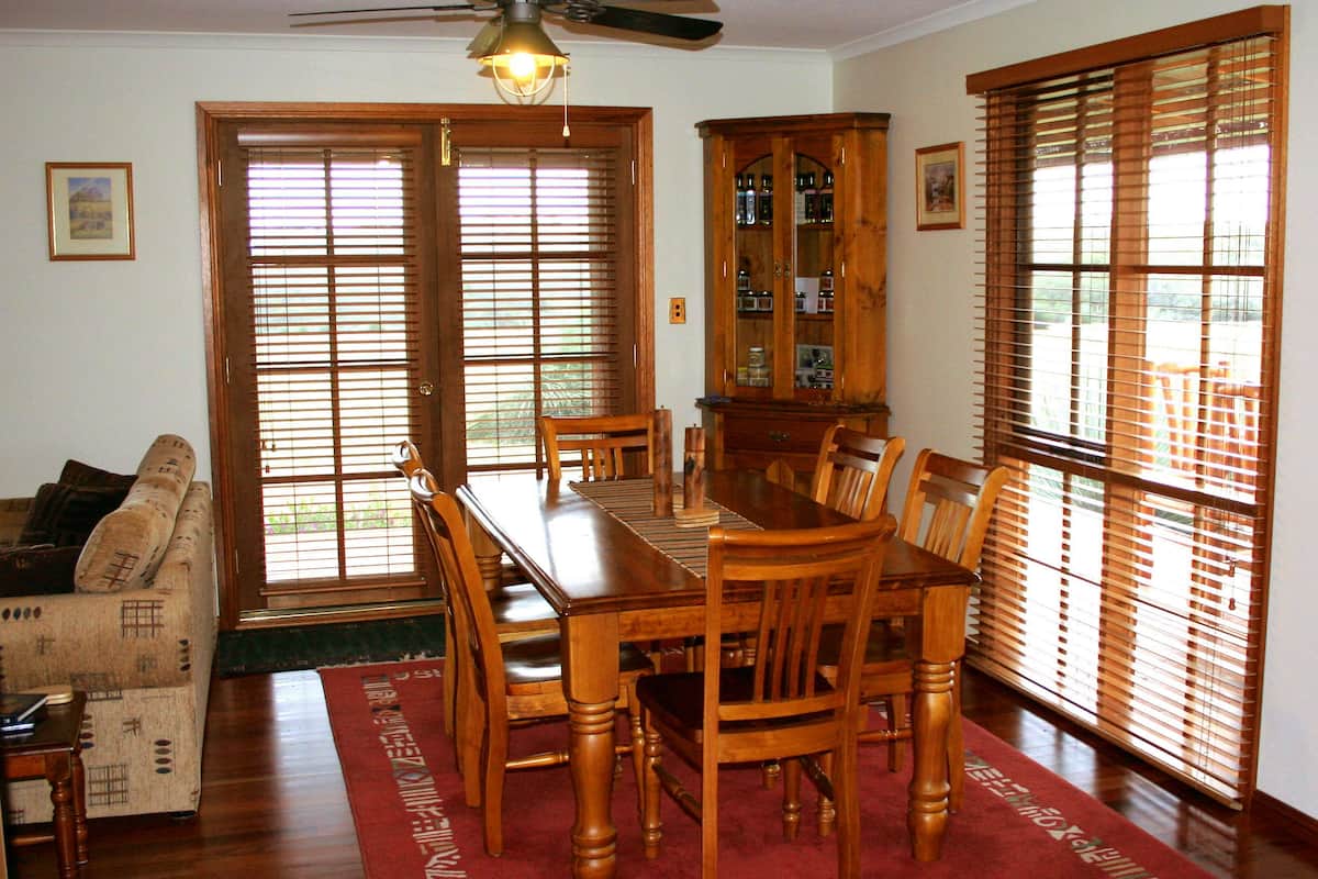 Un comedor con una mesa y sillas de madera, un armario con puertas de vidrio y un ventilador de techo.
