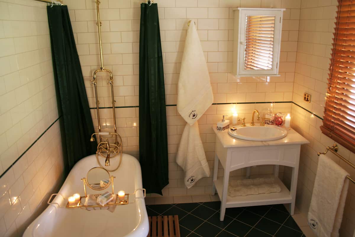 Un baño con bañera, inodoro, lavamanos y ventana con persianas.
