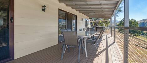 A covered outdoor area with a table and chairs, a glass door, and a view of the landscape.