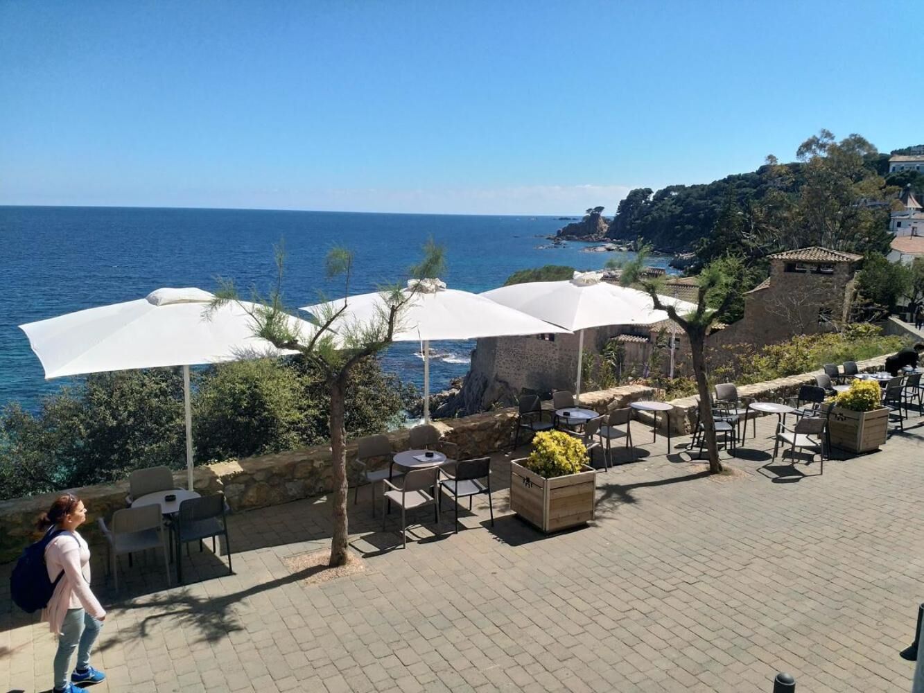 An outdoor patio with tables and chairs, white umbrellas, and a view of the sea.