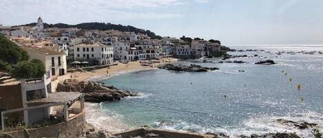 A coastal town with white buildings, a beach, and rocky shoreline.