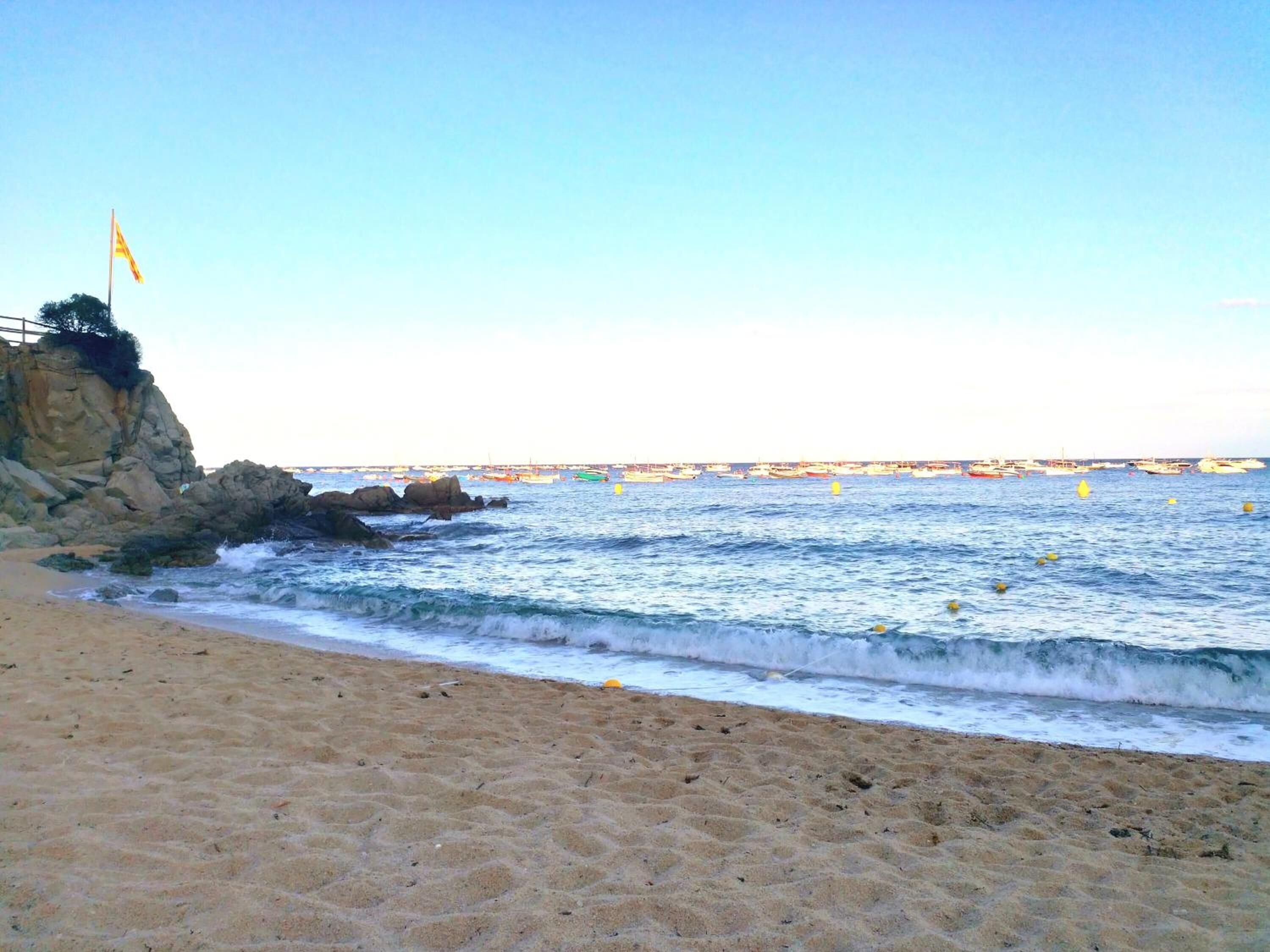 Ein Strand mit einer felsigen Klippe und einer Flagge obenauf.