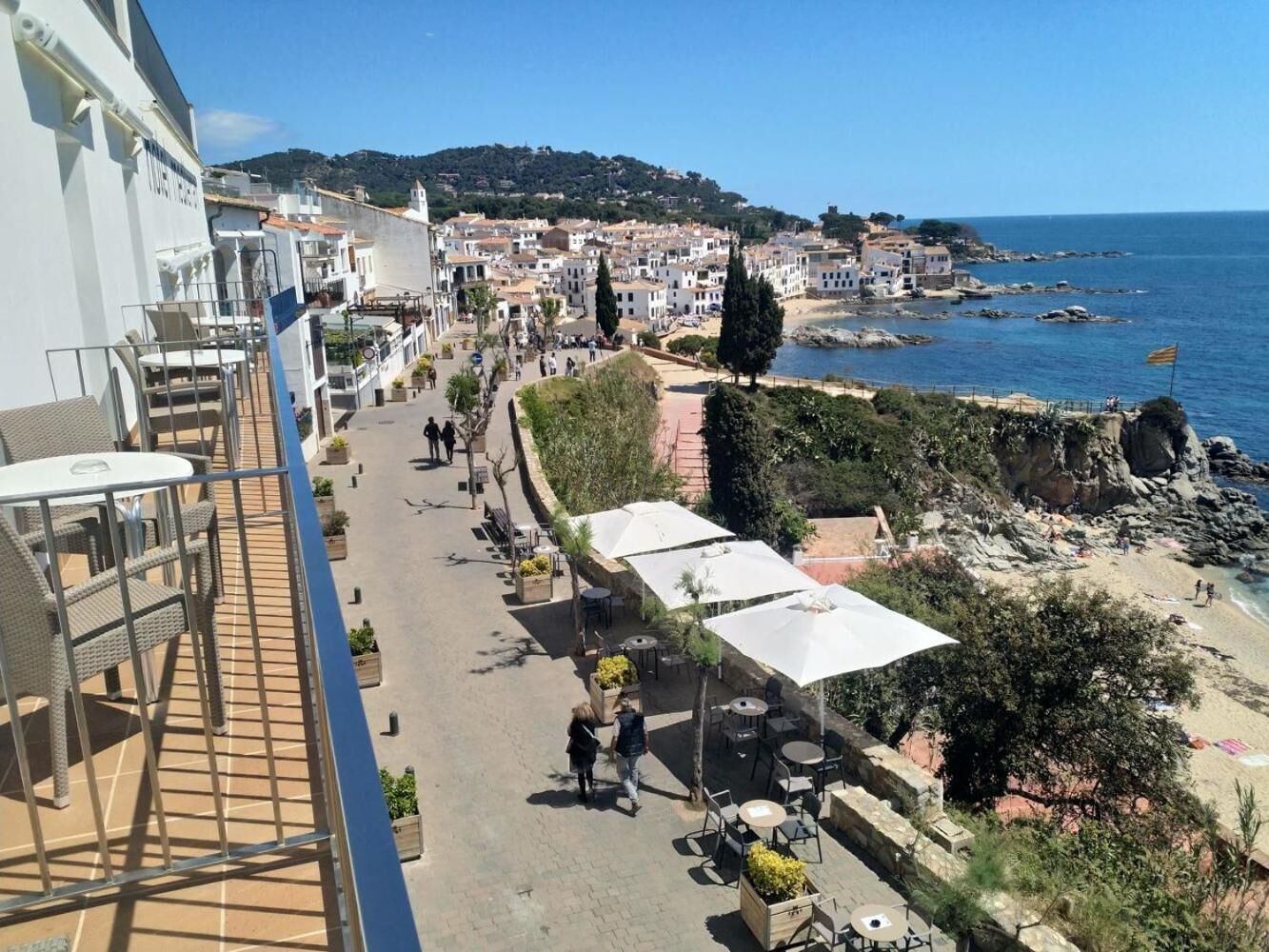 Un balcón con mobiliario exterior que ofrece vistas a un pueblo costero, una playa y acantilados rocosos.