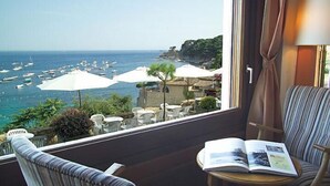 Un balcón con vista al mar, un libro y una silla a rayas.
