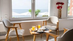 Una mesa con sillas, un jarrón con flores rojas y vistas al mar a través de amplios ventanales.