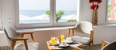 Una mesa con sillas, un jarrón con flores rojas y vistas al mar a través de amplios ventanales.