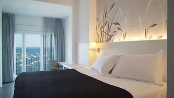 A hotel room with a large bed, a desk, and a view of the sea through the window.