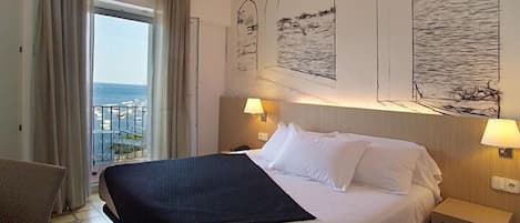 A hotel room with a bed, a chair, a nightstand, and a view of the sea through the window.