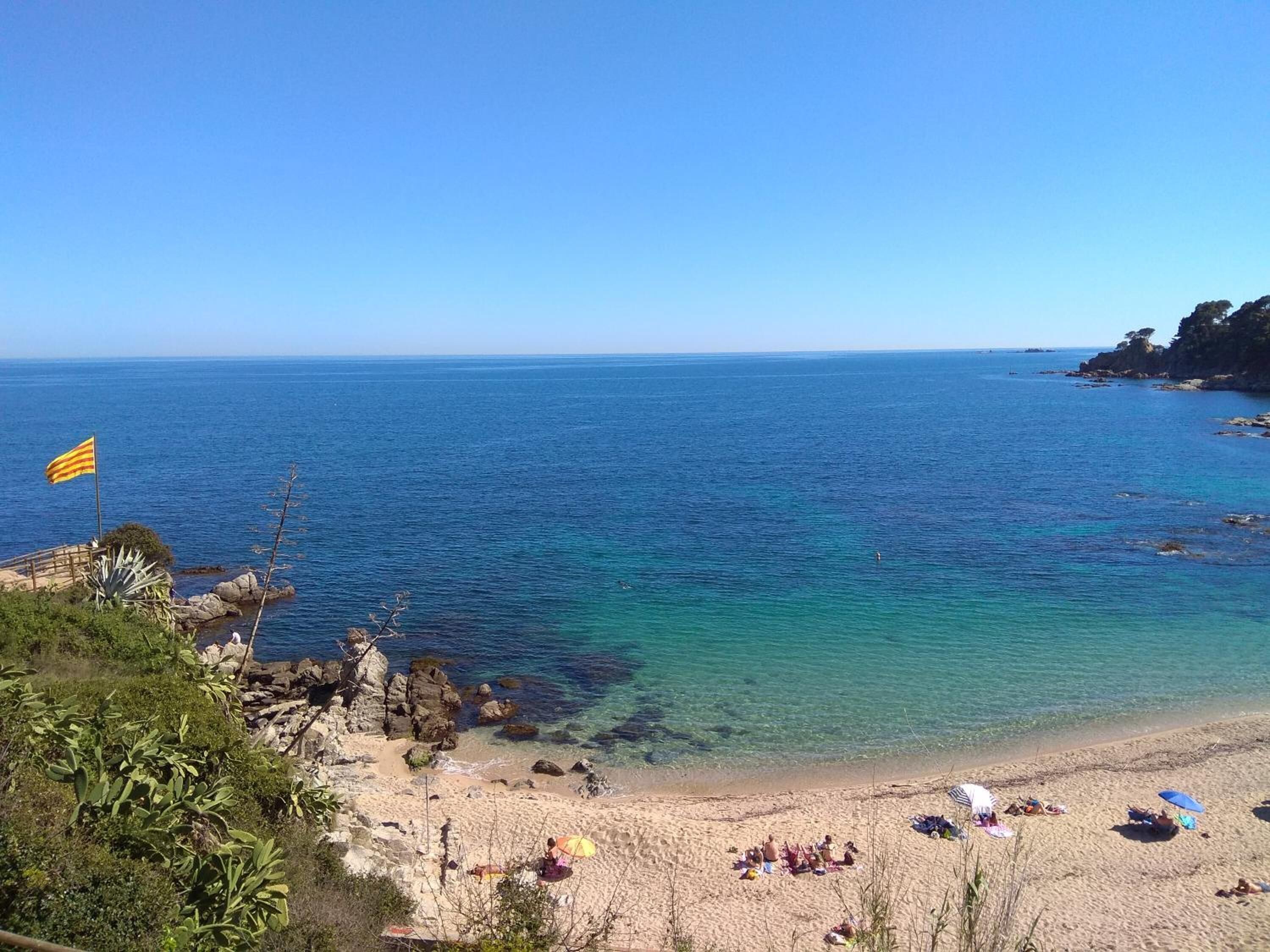 A beach with clear blue water, rocky outcrops, and a flag.