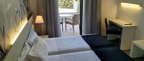 Habitación de hotel con dos camas, un escritorio, una silla y vistas al exterior.
