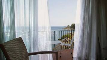 A balcony with a wicker chair and a table, overlooking a rocky coastline.