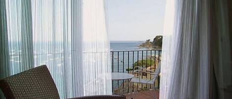 Un balcón con una silla de mimbre y una mesa, con vistas a una costa rocosa.