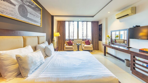 Hotelkamer met een groot bed, twee fauteuils, een bijzettafeltje, een televisie en een schilderij aan de muur.