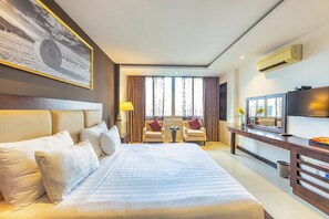 Hotelkamer met een groot bed, twee fauteuils, een bijzettafeltje, een televisie en een schilderij aan de muur.
