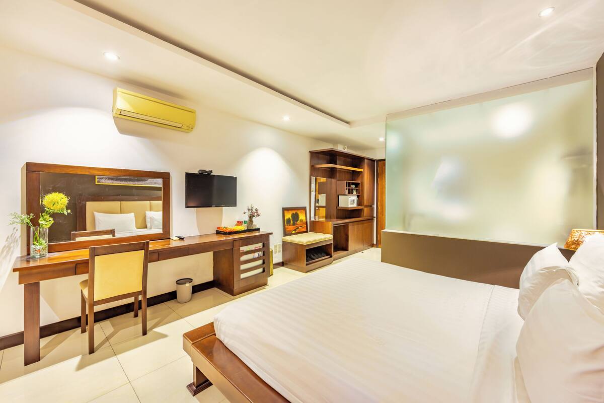 A modern hotel room with a large bed, a desk with a chair, a TV, and a built-in wardrobe.