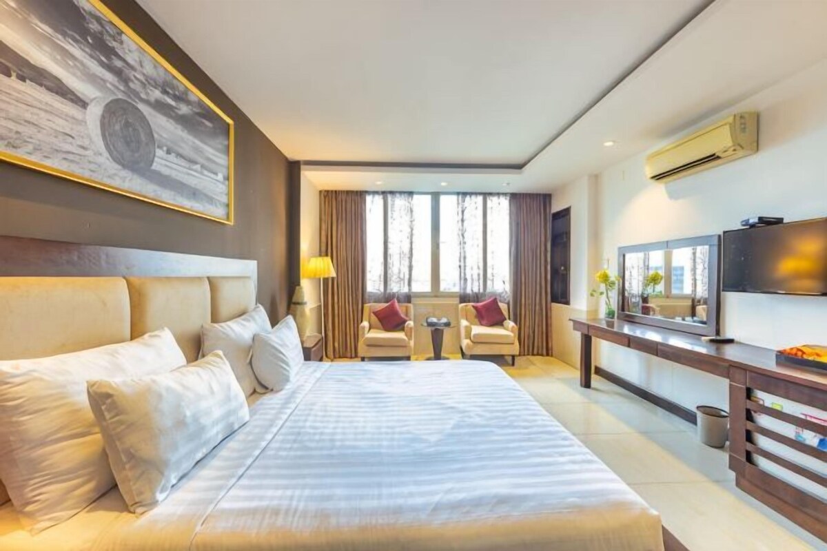 A hotel room with a large bed, a TV, a desk with a chair, and a window with curtains.