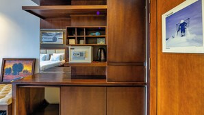 Een kleine hotelkamer met een houten bureau, een bed, een magnetron en een ingelijste foto aan de muur.