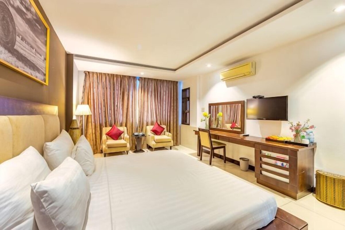 A hotel room with a large bed, a desk, a chair, a TV, and a window with curtains.