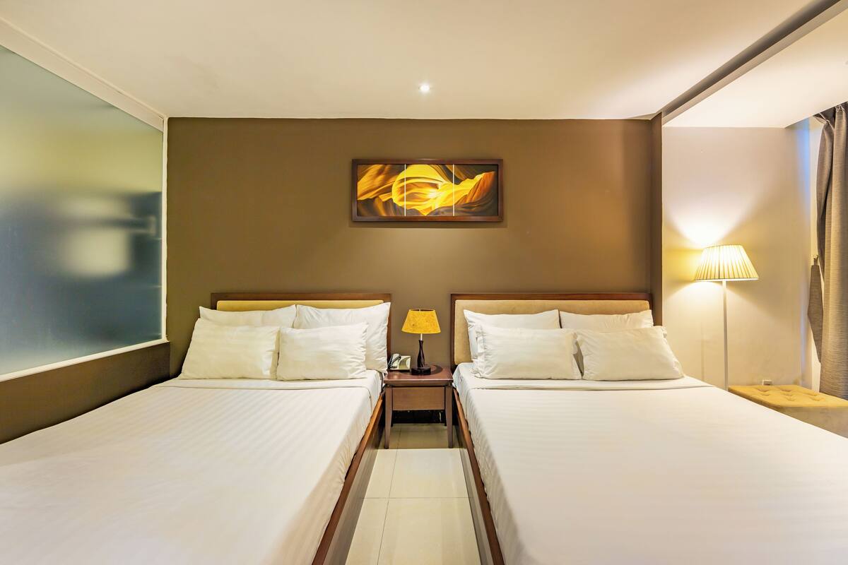 A hotel room with two beds, a nightstand with a lamp, and a painting on the wall.