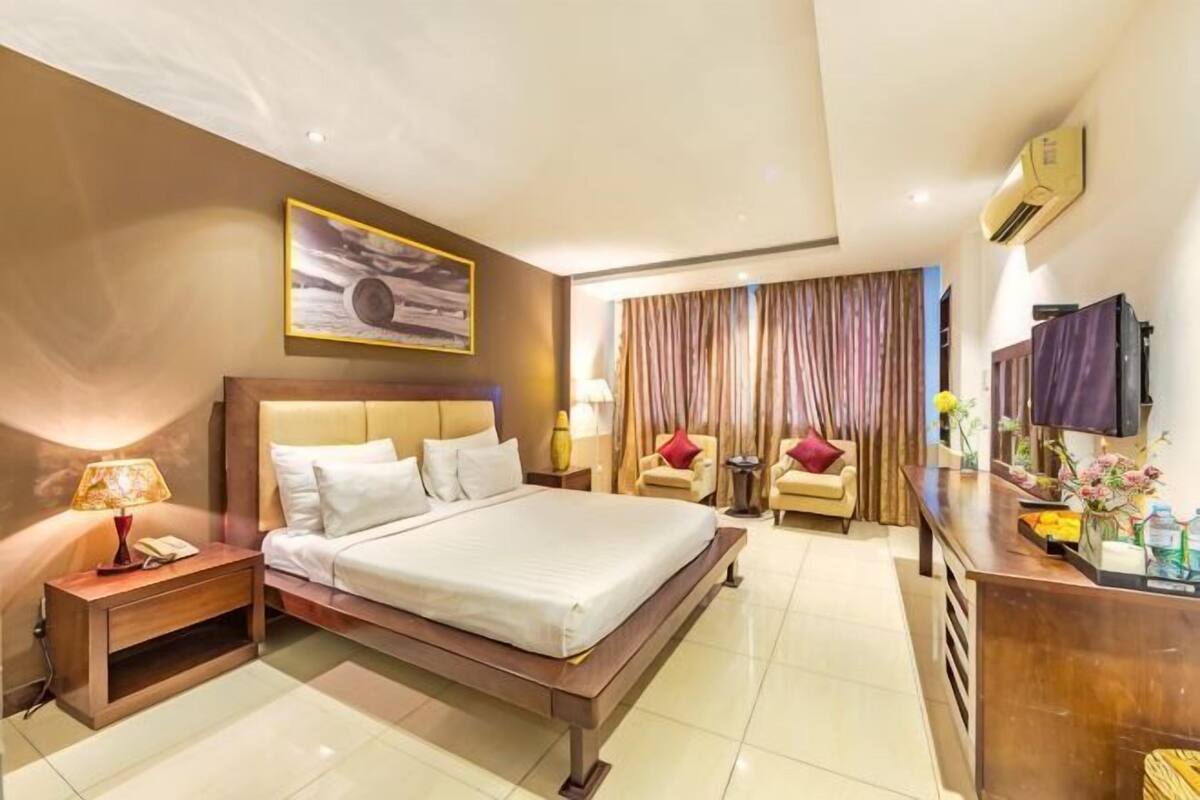 A hotel room with a large bed, bedside tables, a desk, a TV, and a window with curtains.
