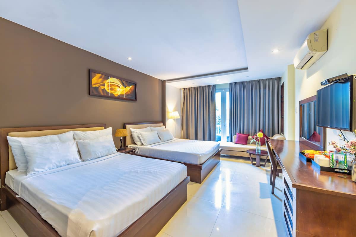 A hotel room with two beds, a desk, a TV, and a window with curtains.