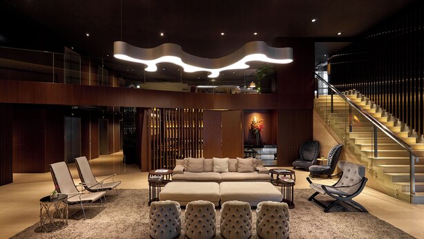Un hall d’entrée spacieux, doté d’un canapé moderne, de fauteuils, de poufs et d’un escalier.