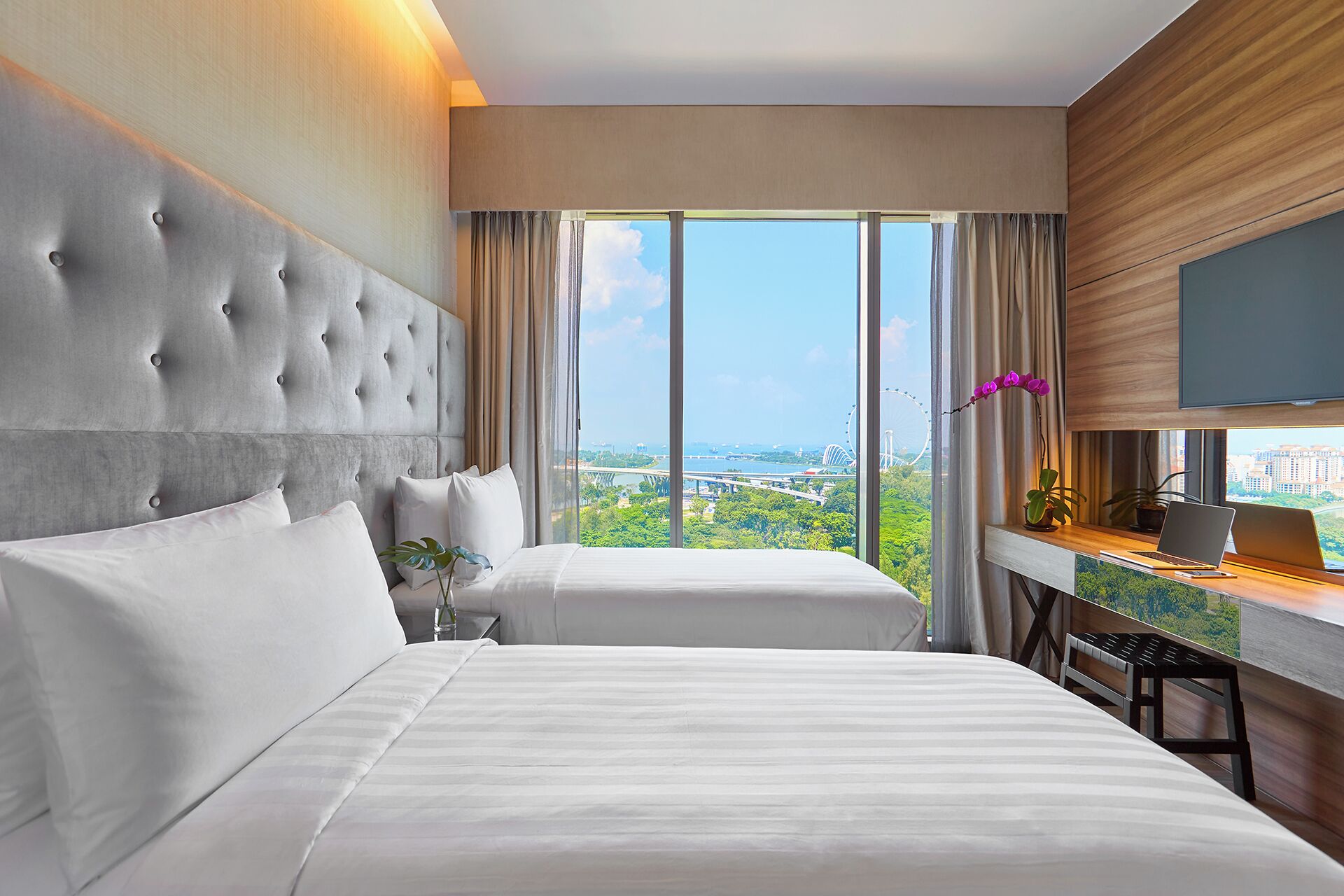 A hotel room with a large bed, a desk with a laptop, and a view of a cityscape.