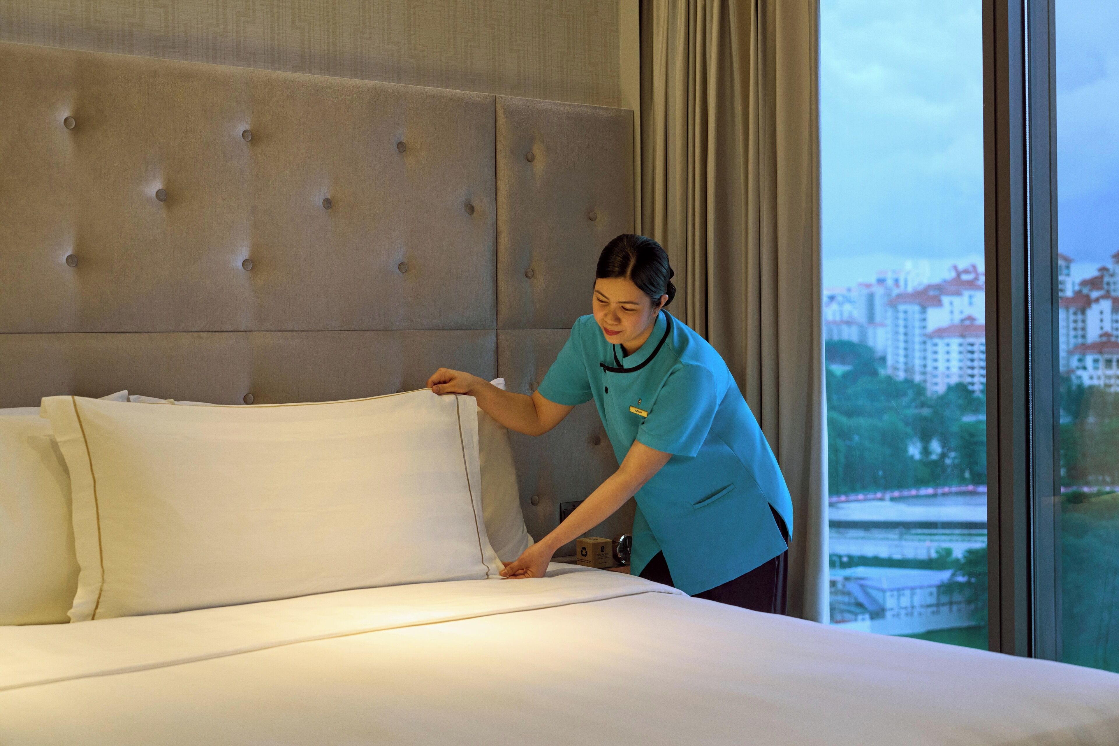 Habitación de hotel con un gran cabecero capitonado, una cama bien hecha y vistas a edificios a través de la ventana.