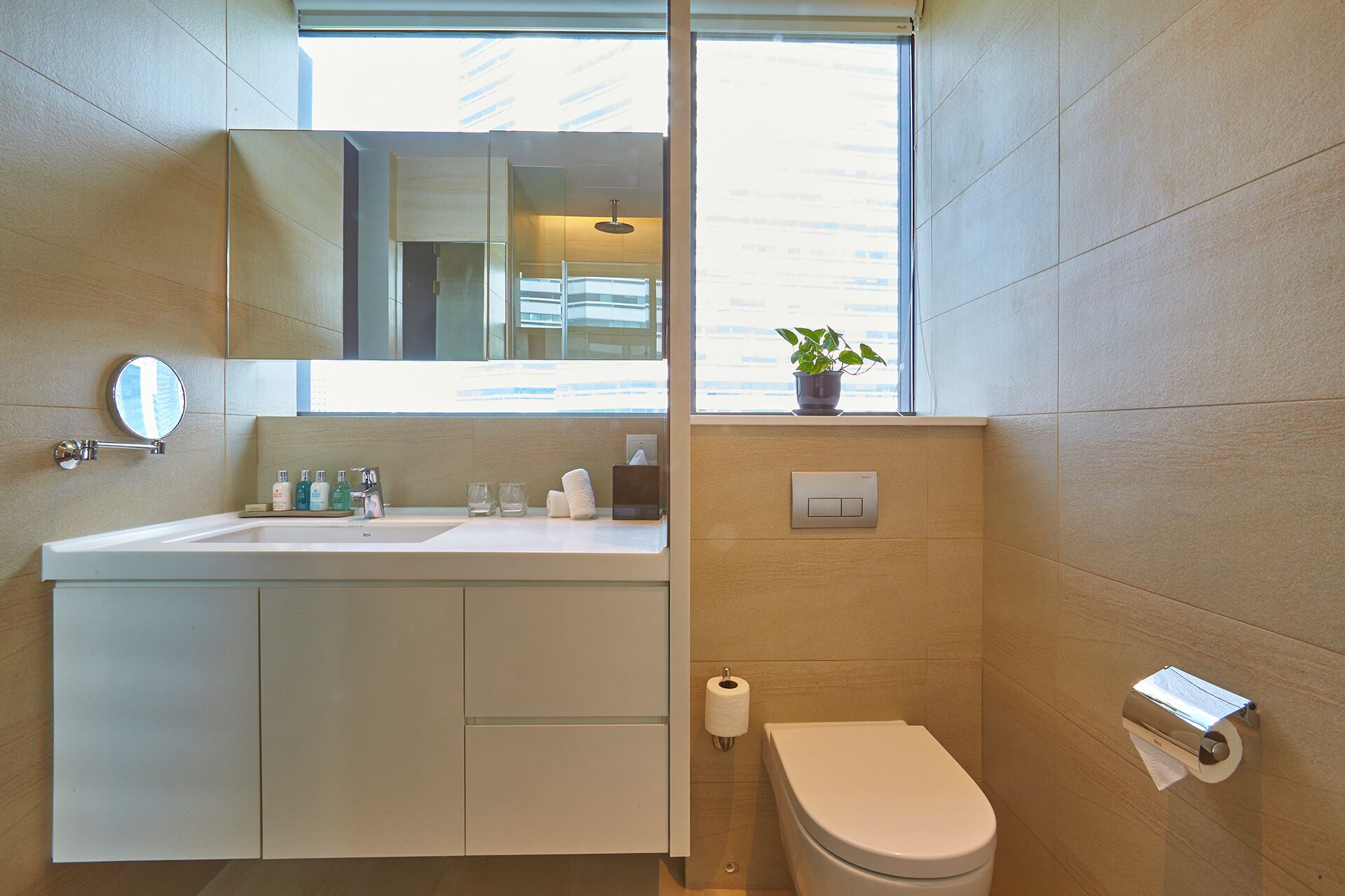 A modern bathroom with a sink, mirror, toilet, and a window with a plant on the windowsill.