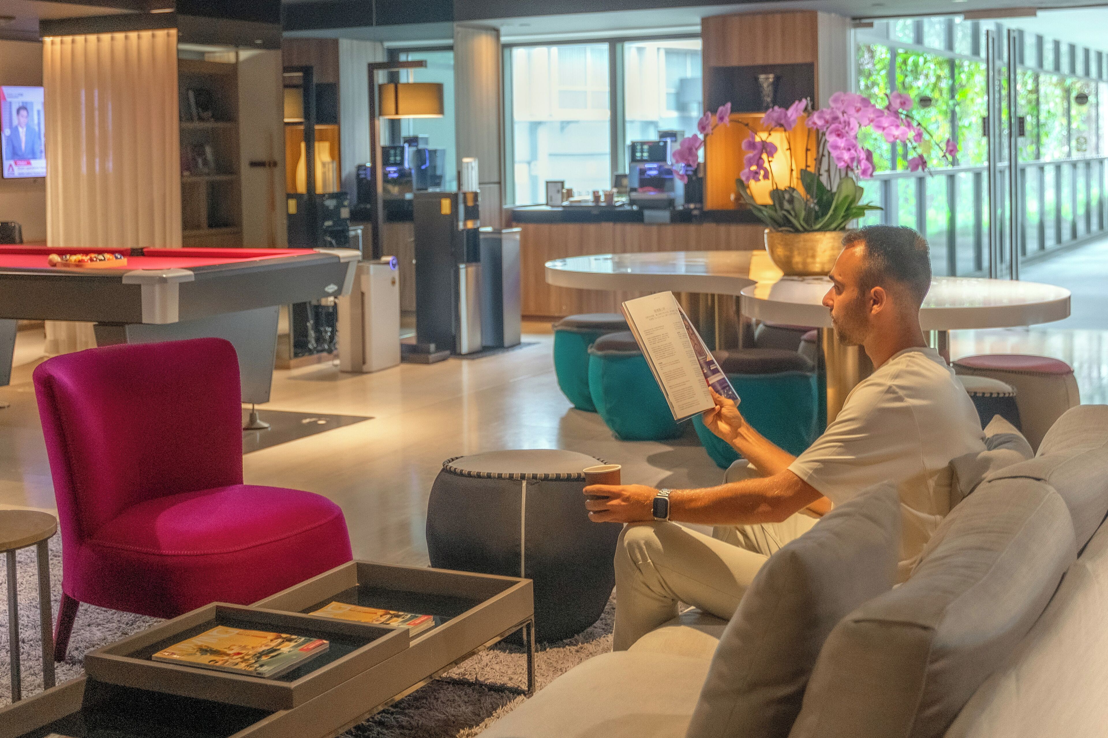 A modern lounge area with a pool table, comfortable seating, and a coffee table with magazines.
