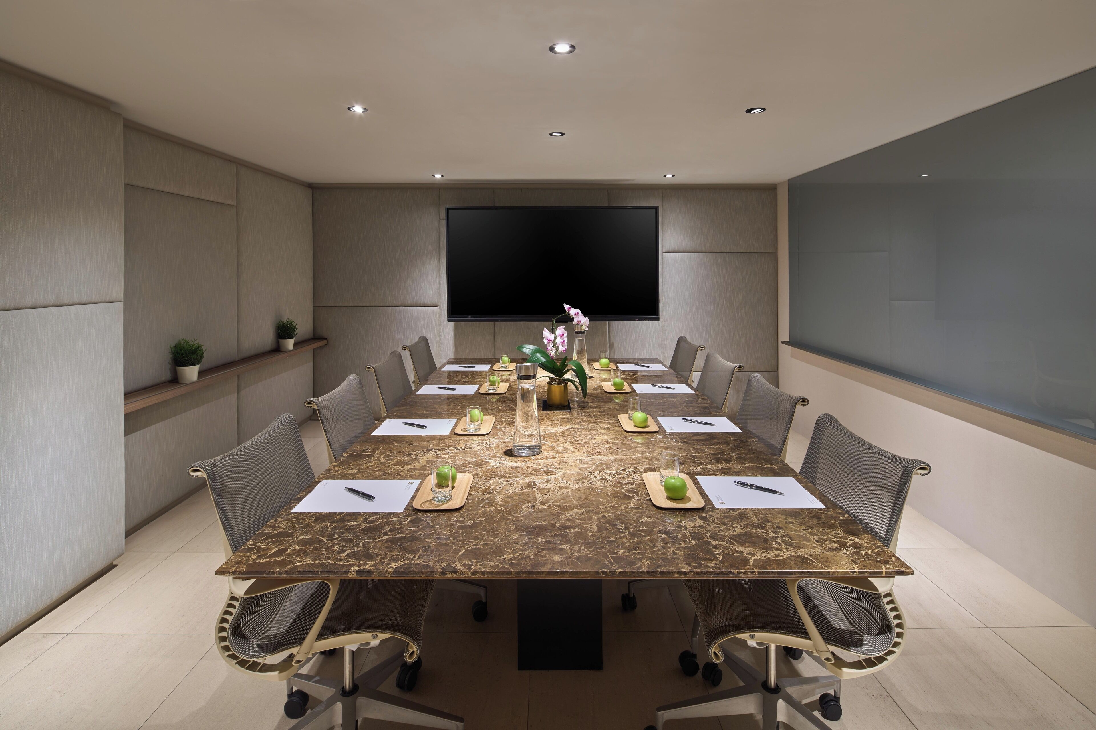 A conference room with a marble table, chairs, a large screen, and potted plants.