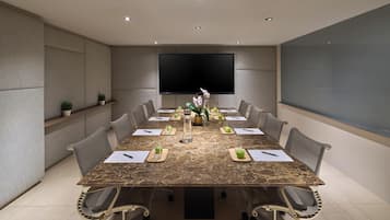 Un salón de conferencias con una mesa de mármol, sillas, una pantalla grande y plantas en macetas.