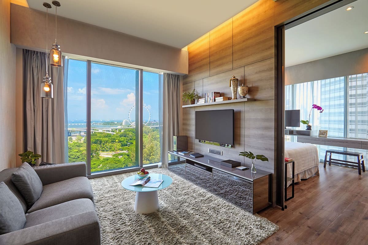 Een moderne woonkamer met een grote televisie, comfortabele zitplaatsen, een salontafel en uitzicht op een stadsbeeld en groen.