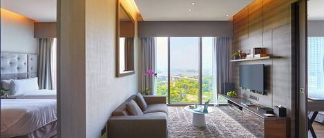 Una habitación de hotel moderna con una cama grande, un sofá, un televisor y vistas a un paisaje urbano.