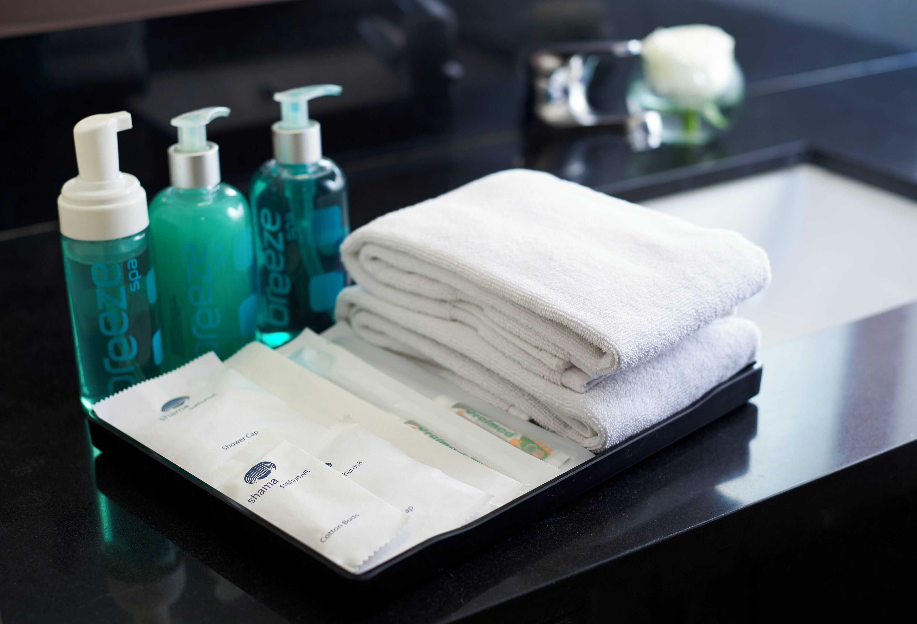 Una encimera de baño con una pila de toallas blancas, una bandeja negra y tres botellas de jabón corporal Breeze.