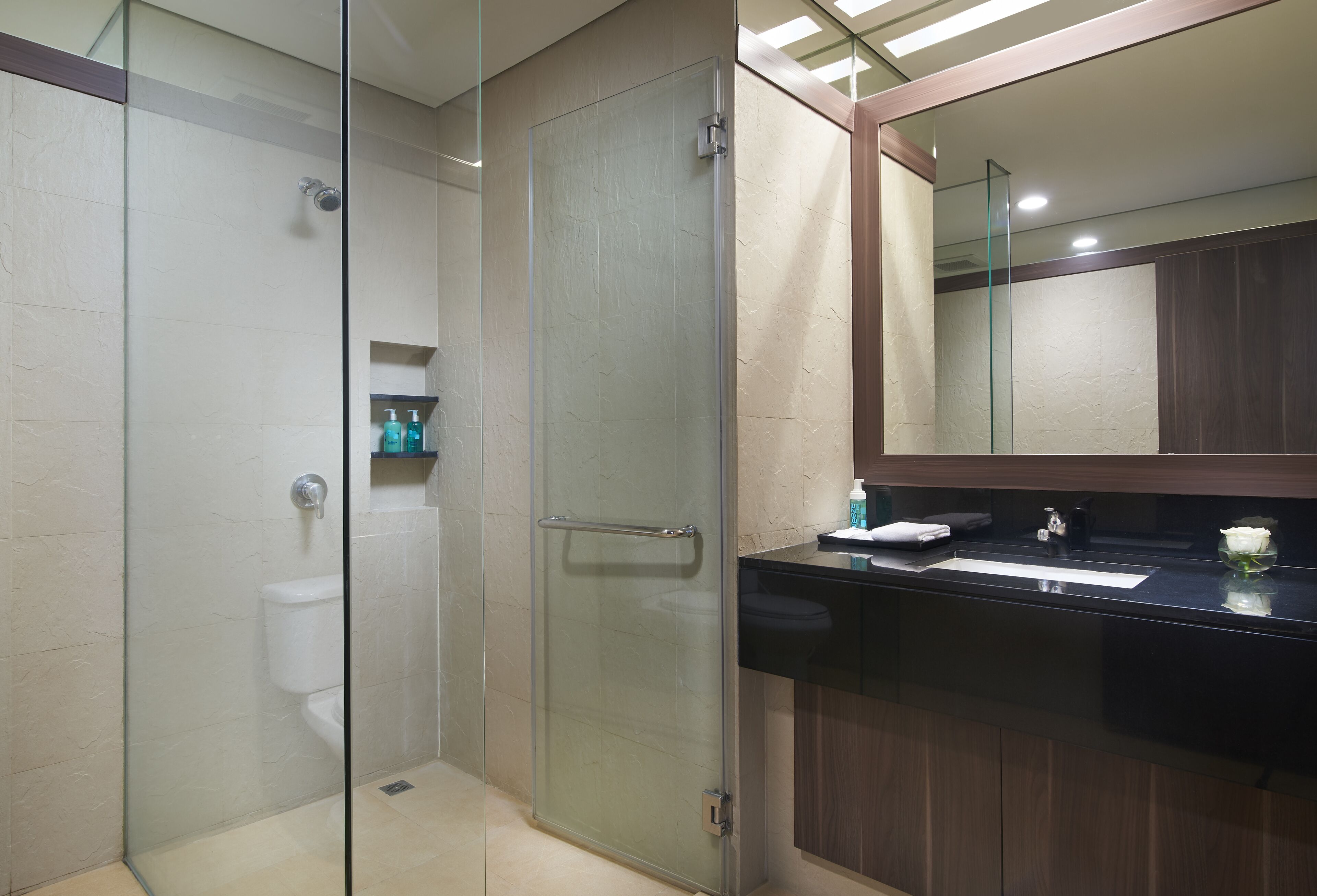A modern bathroom with a glass shower enclosure, a black sink, and a wooden vanity.
