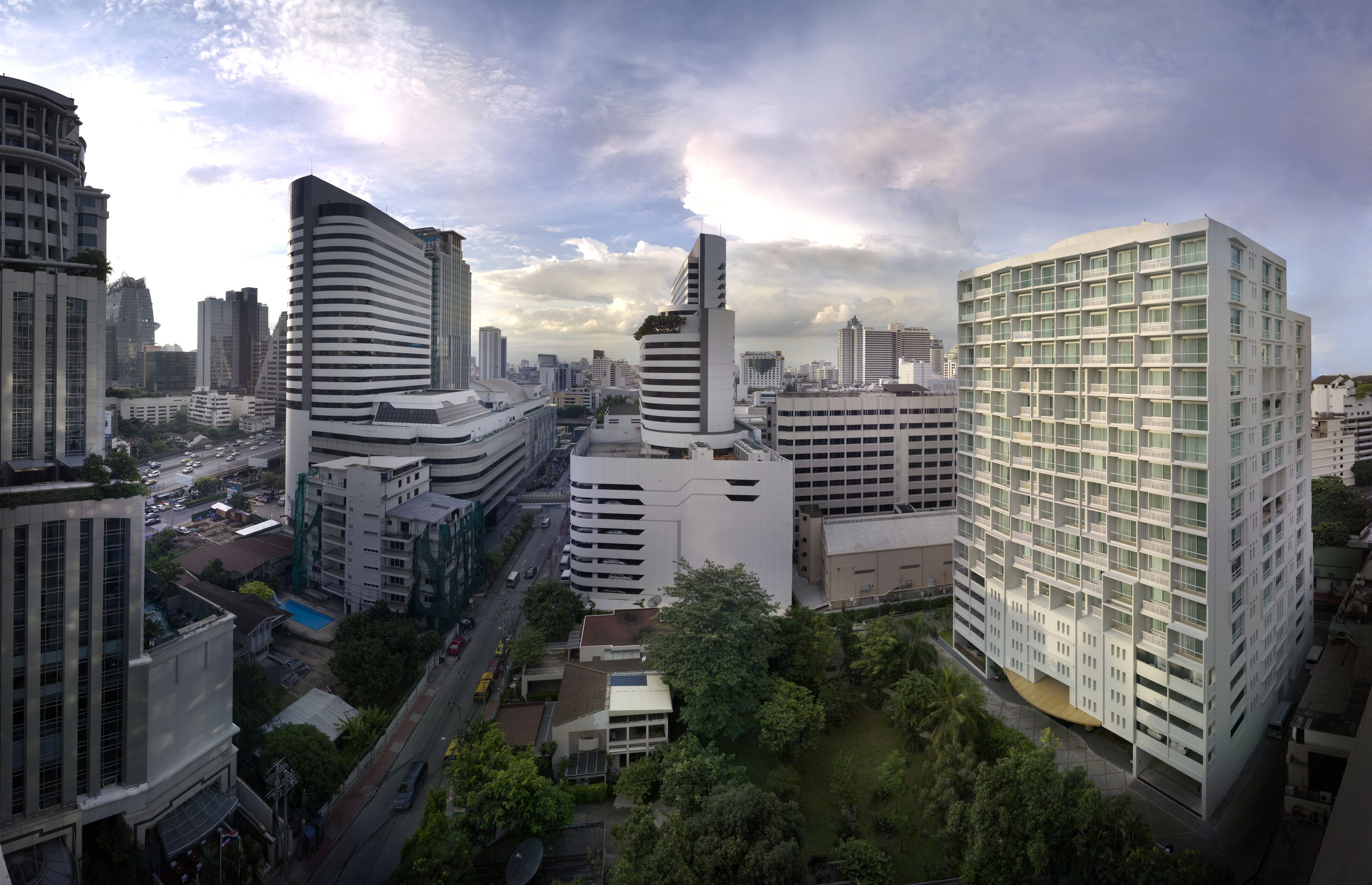 A modern cityscape with high-rise buildings, including a distinctive curved building and a large white building with a grid-like facade.