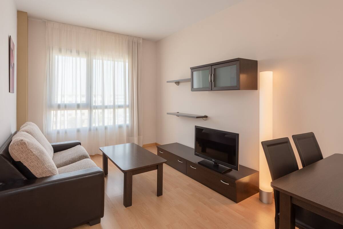 Ein modernes Wohnzimmer mit Sofa, Couchtisch, Fernseher und Essbereich mit Stühlen.