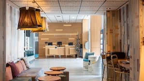 Un moderno vestíbulo de hotel con mostrador de recepción, zona de estar y bar/lounge con taburetes y mesas.