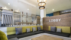 Un vestíbulo moderno con un sofá seccional, una mesa de centro de madera y un cartel que dice 'Lobby' en la pared.