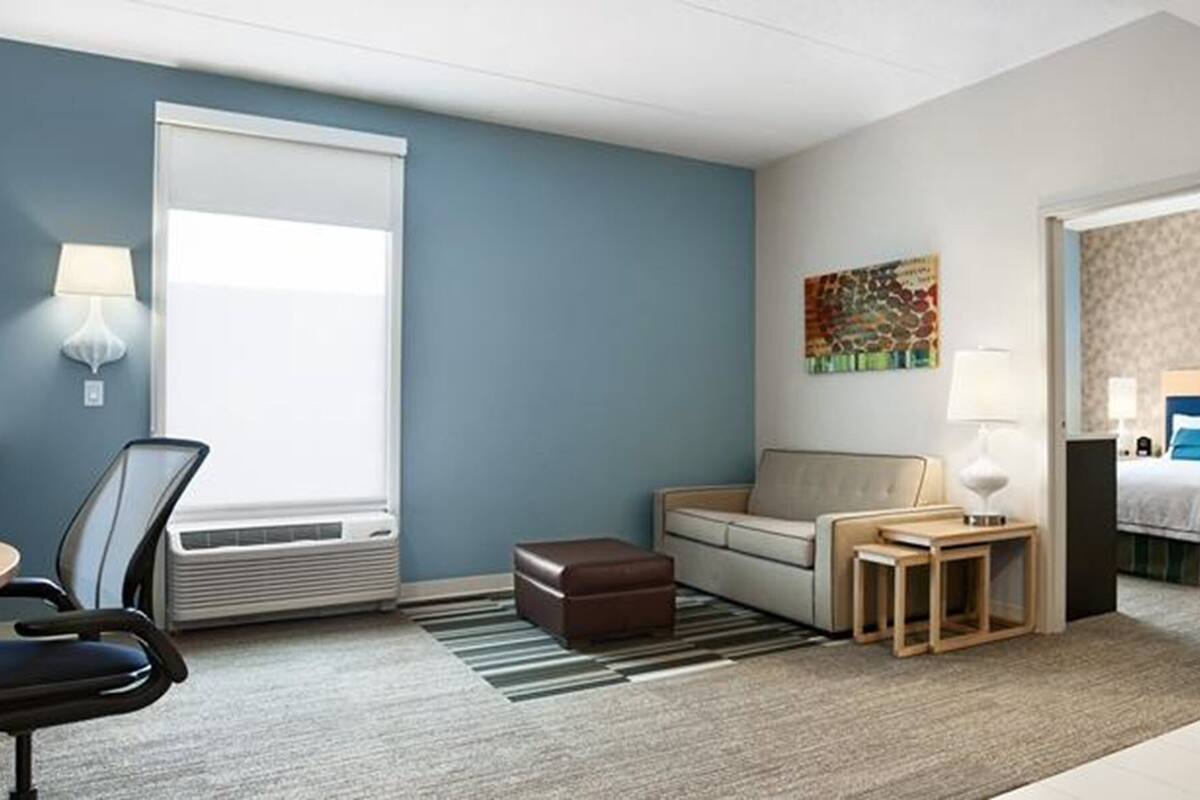 Ein Hotelzimmer mit Schreibtisch, Stuhl, Sofa und einem kleinen Tisch mit Lampe.