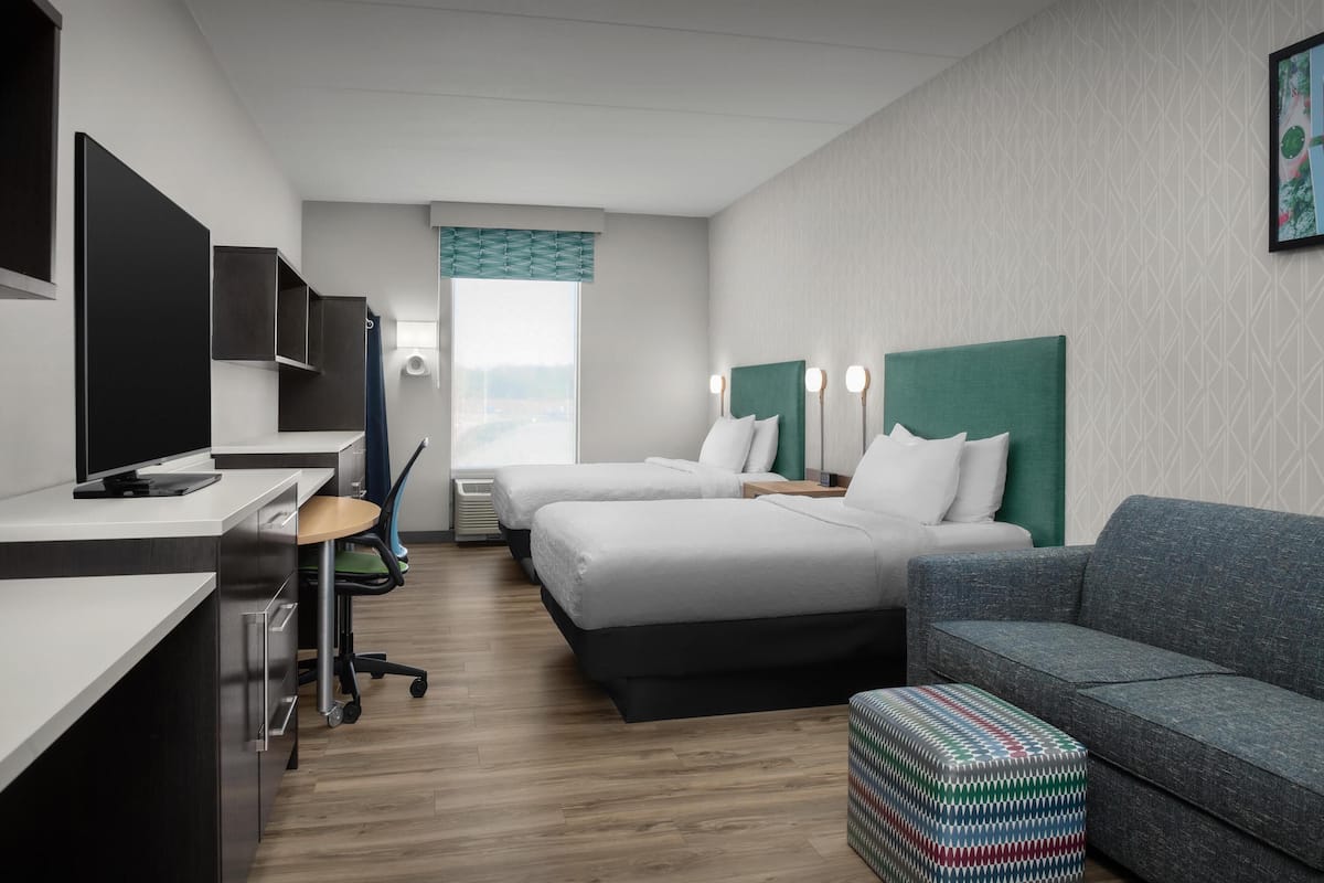 Ein Hotelzimmer mit zwei Betten, einem Schreibtisch mit Computer, einer Couch und einem kleinen Hocker.