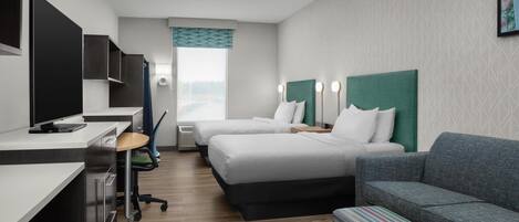 Une chambre d’hôtel avec deux lits, un bureau avec un ordinateur, un canapé et un petit pouf.